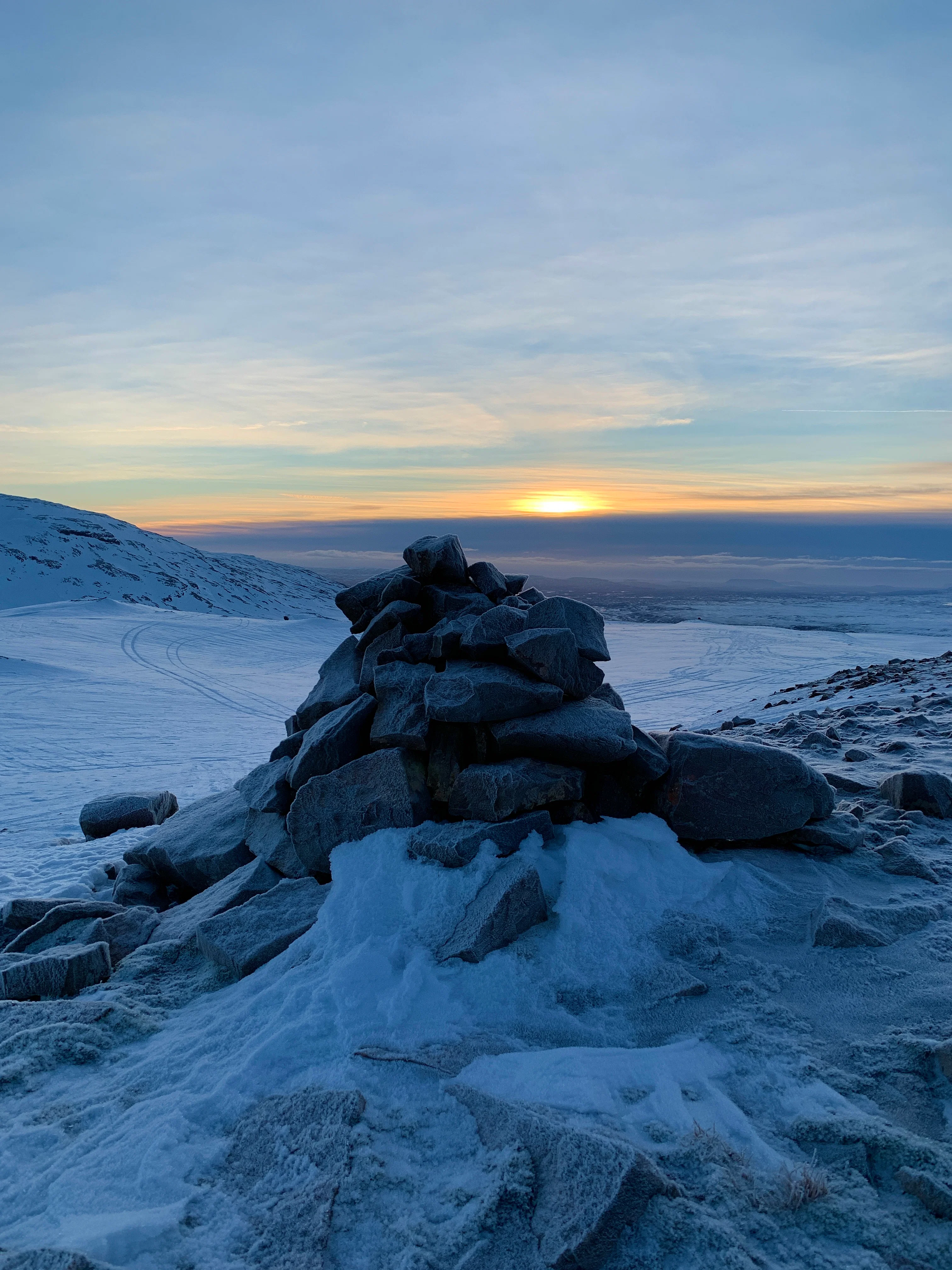 Sunrise view over a snowy mountain landscape with a rock cairn in the foreground.